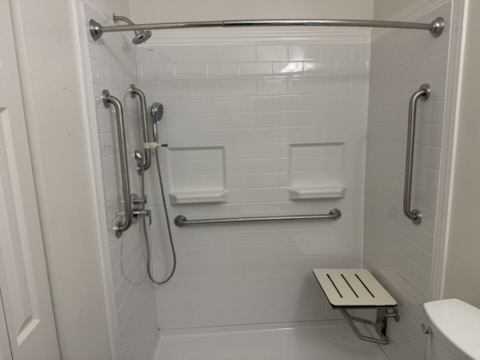 Accessible tiled shower with vertical and horizontal grab bars and a fold-down seat, installed by Indypendent Living