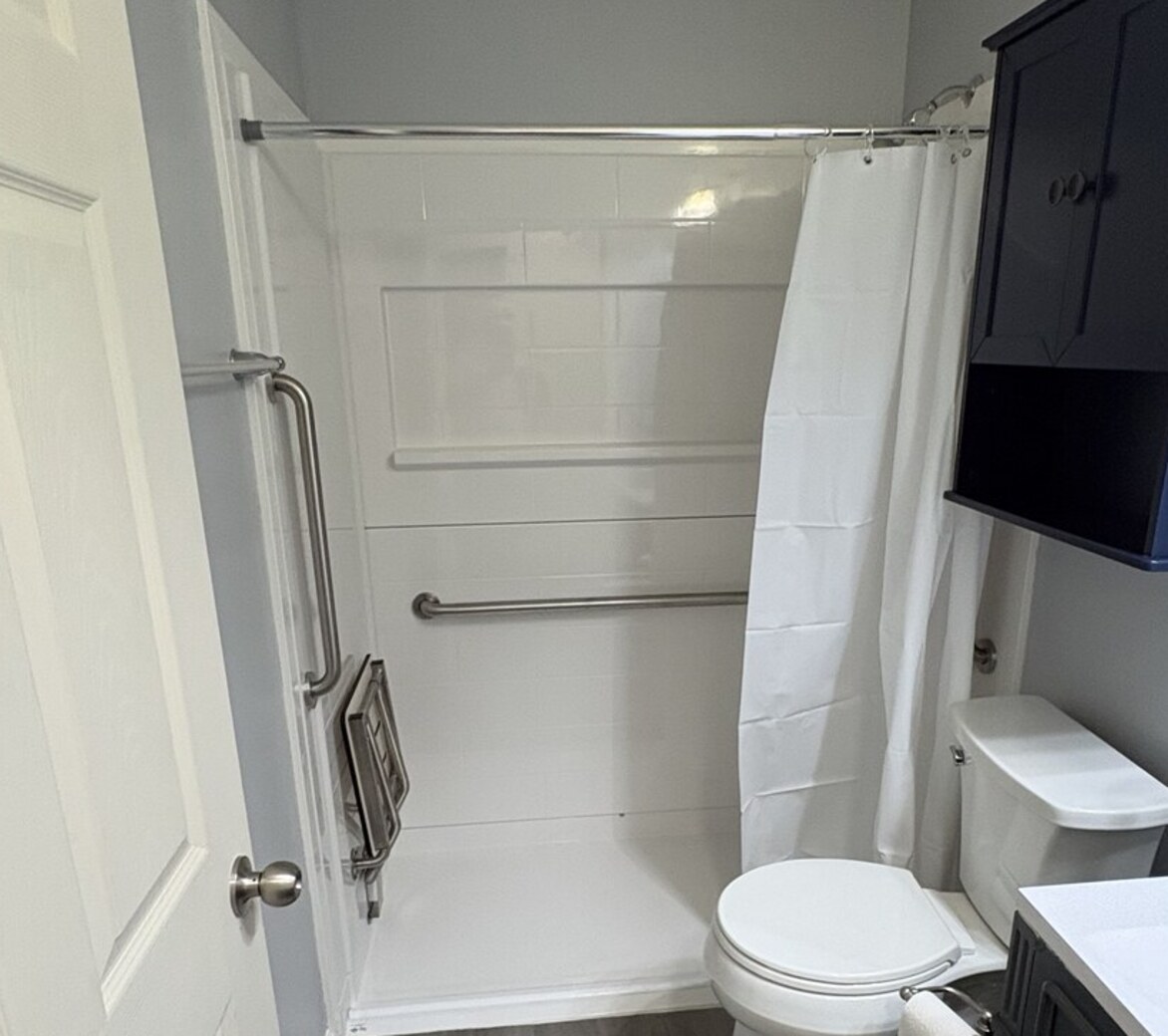 Compact central Indiana bathroom fitted with a walk-in shower, fold-down seat, and a toilet support rail between the toilet and vanity